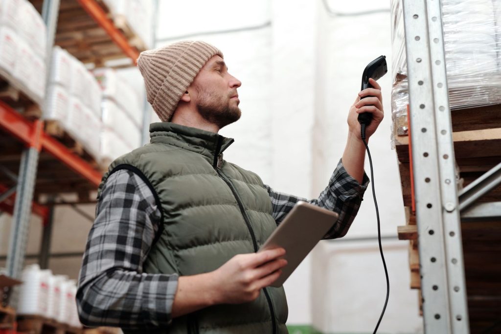 Warehouse worker scanning a barcode on a carton with a handheld scanner and tablet